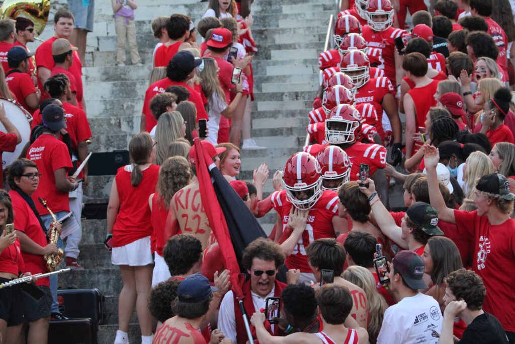 Football players walking down steps, high fiving students